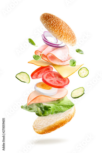 Sandwich with flying ingredients isolated on a white background. Layered delicious bagel, ham, cheese and fresh vegetables photo