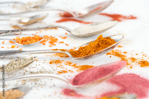 selective focus of colorful bright spices in silver spoons on white background