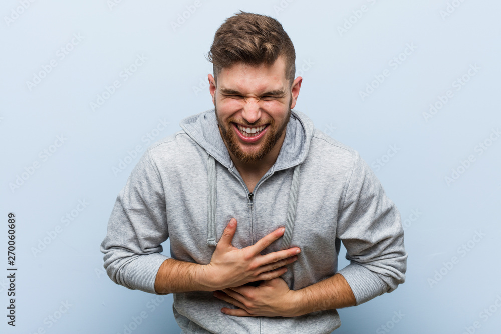 Young handsome fitness man laughs happily and has fun keeping hands on stomach. Young handsome fitness man laughs happily and has fun keeping hands on stomach.