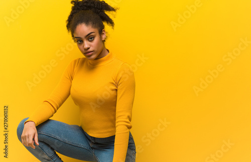Young black woman sitting over an orange wall © Asier