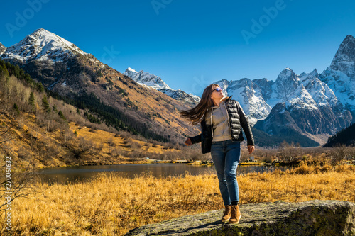 Beautiful young russian woman in front of autumn landscape with mountain lake Tumanly-kel, the Mist lake, located in Russia, near Dombay , in Caucasus mountains, Gonachkhir gorge