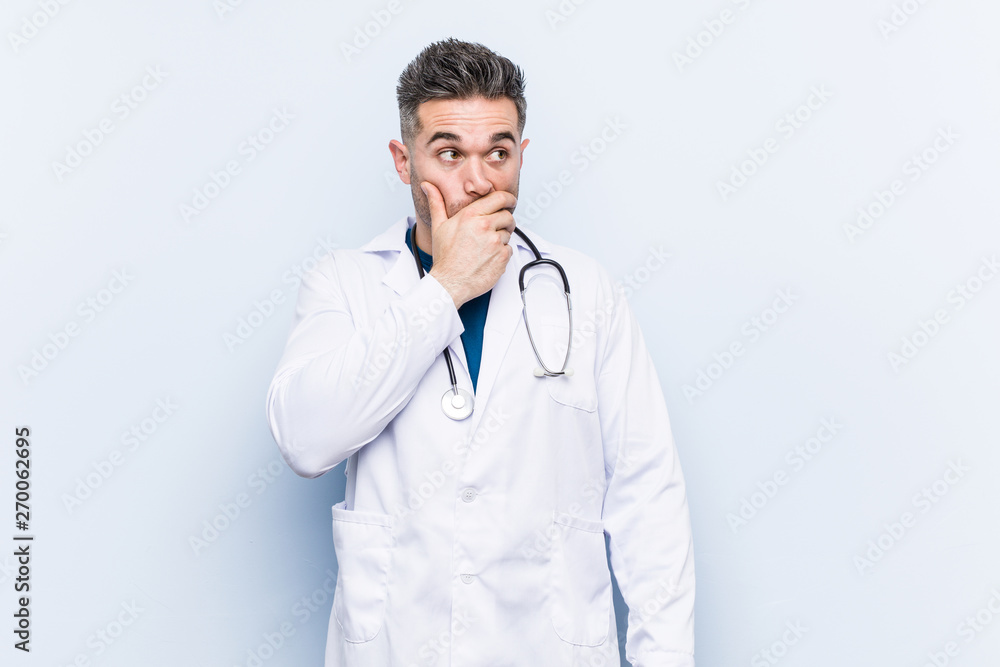 Young handsome doctor man thoughtful looking to a copy space covering mouth with hand. Young handsome doctor man thoughtful looking to a copy space covering mouth with hand.