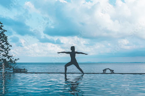 silhouette woman practice yoga Warrior one pose to meditation summer vacation on the pool above the beach Travel in tropical beach Thailand vacations and relaxation Concept