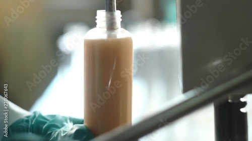 Laboratory assistants filling up bottle with body care lotion or shampoo in factory