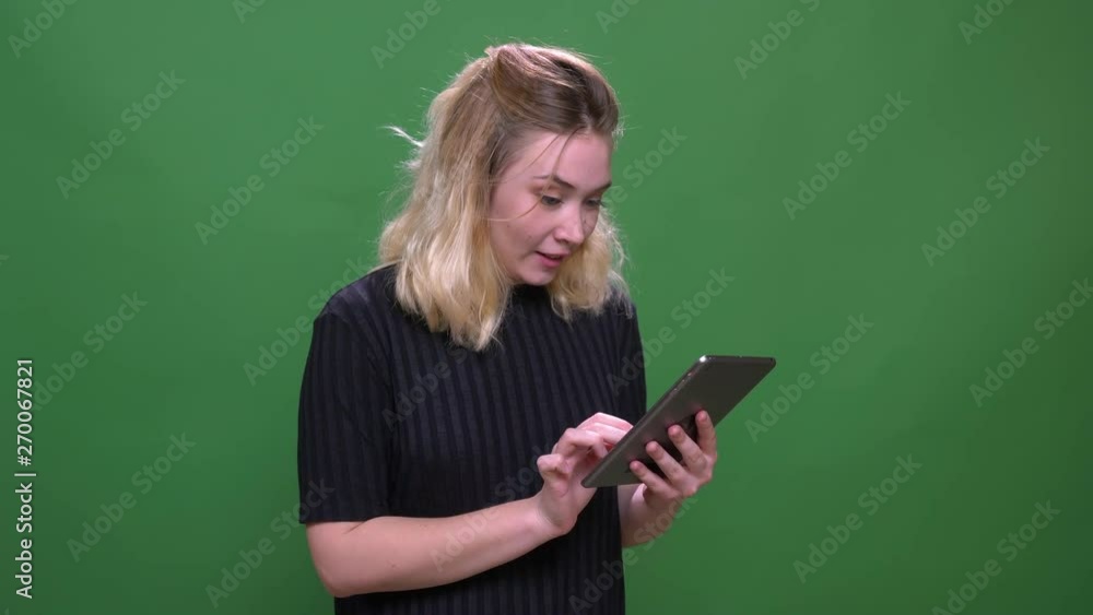 Closeup portrait of young pretty blonde caucasian female using the tablet with background isolated on green Closeup portrait of young pretty blonde caucasian female using the tablet with background isolated on green