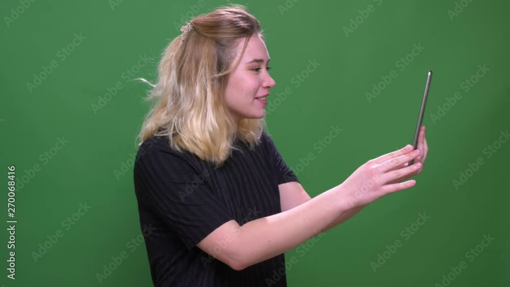 Closeup portrait of young pretty blonde caucasian female having a video call on the tablet with background isolated on green