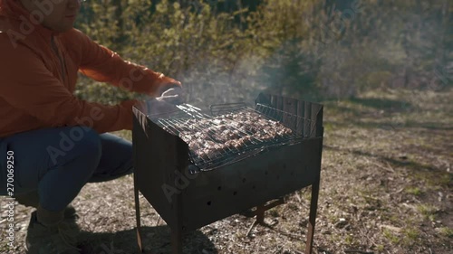 A man roasts a meat barbecue of pork or beef on charcoal on a Sunny summer day. A picnic on the weekend cooking delicious food outdoors photo