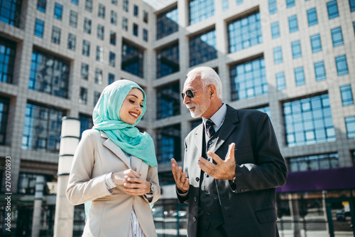 Photography Young beautiful muslim woman with hijab standing in front of modern city building and talking with senior business man