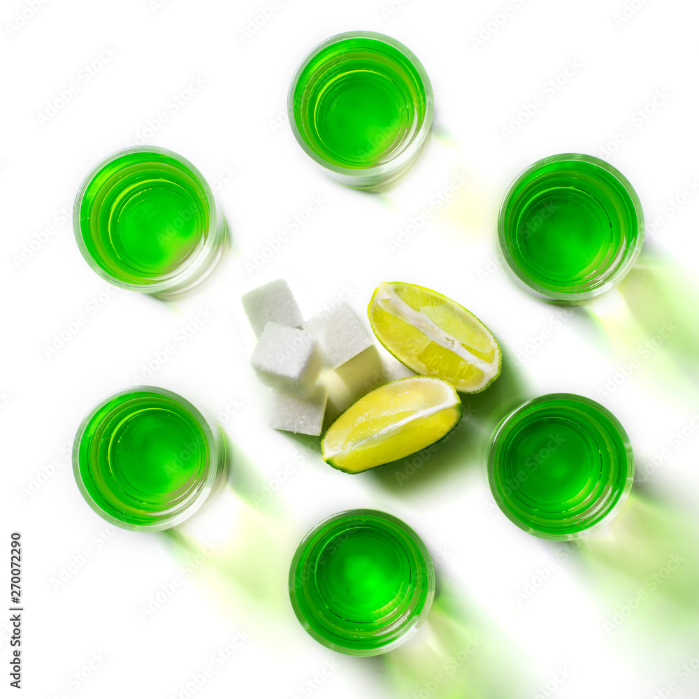 Absinthe green liquor in glasses. Alcoholic hallucinogenic beverage. White background. Pieces of lime and white sugar. Flat lay Absinthe green liquor in glasses. Alcoholic hallucinogenic beverage. White background. Pieces of lime and white sugar. Flat lay