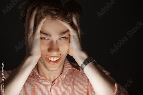 Close-up portrait of attractive kind young anger man rolled his eyes and clutching his head with his hands. Isolated on black background and looking at camera. Depression or fear concept. photo