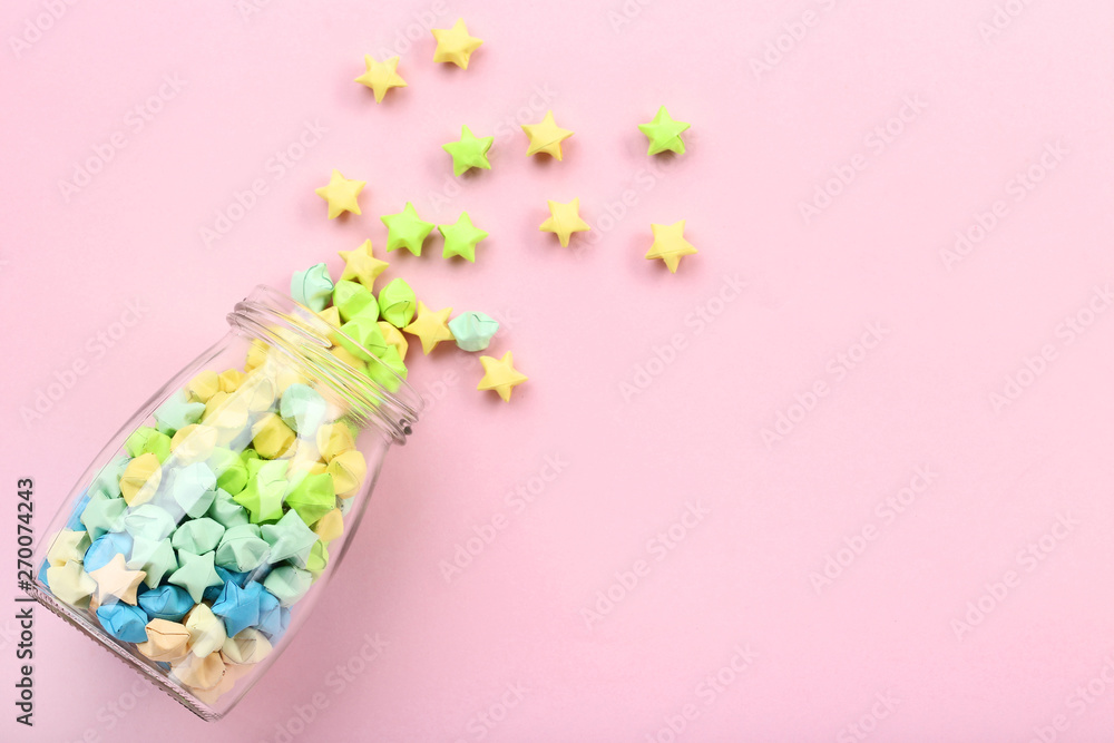 Colorful paper stars in glass jar on pink background