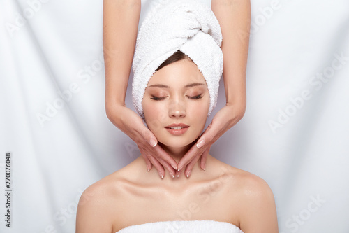 beautician massaging neck of woman in bath towel and with naked shoulders, facial procedures in spa for pretty girl