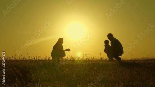 mother and Dad play with their daughter in sun. happy baby goes from dad to mom. young family in the field with a child 1 year. family happiness concept. beautiful sunshine  sunset.