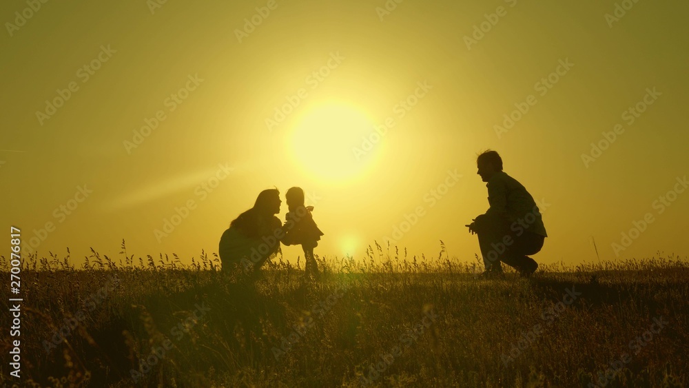 mother and Dad play with their daughter in sun. happy baby goes from dad to mom. young family in the field with a child 1 year. family happiness concept. beautiful sunshine, sunset.