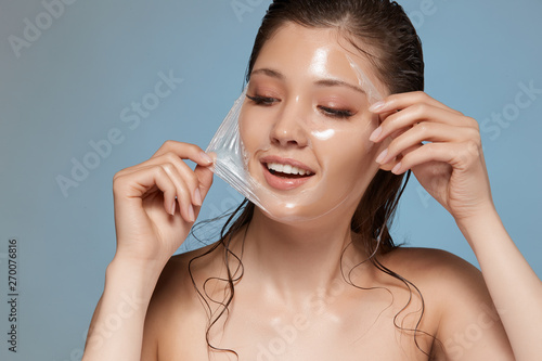 young and beautiful woman removes facial trasparent mask and smiles, perfect fresh face with cosmetology treatment