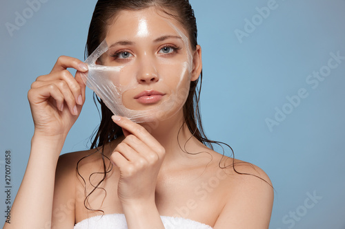 Obraz na płótnie attractive woman removing moisturizing mask and looking to the camera, copy space, cosmetology for face, young female face after procedures w salonie