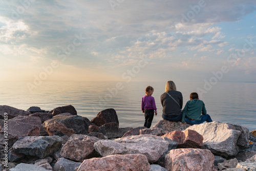 family woman with children sitting on a rock on the beach at sunset