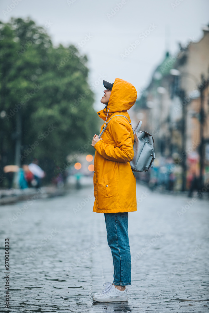 side view of woman in yellow raincoat standing on city street foto de Stock Adobe Stock