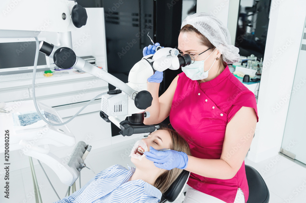 A female professional dentist examines a female patient with a stamotologic microscope in her office. Stamotologist profession concept A female professional dentist examines a female patient with a stamotologic microscope in her office. Stamotologist profession concept