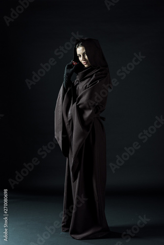 full length view of woman in death costume holding dice on black