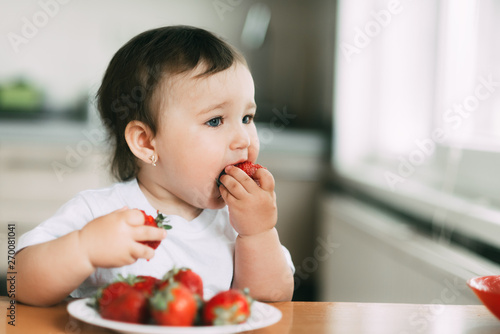 Little girl child in white t-shirt eating strawberries all smeared and dirty