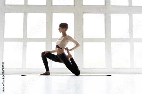 Young attractive woman practicing yoga, standing in Horse rider exercise, anjaneyasana pose, working out, wearing sportswear, cool urban style.