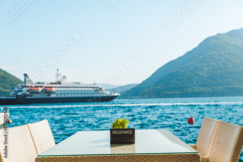 cafe table on beach with beautiful view of sea and mountains. reserved plate on it. cruise liner on background