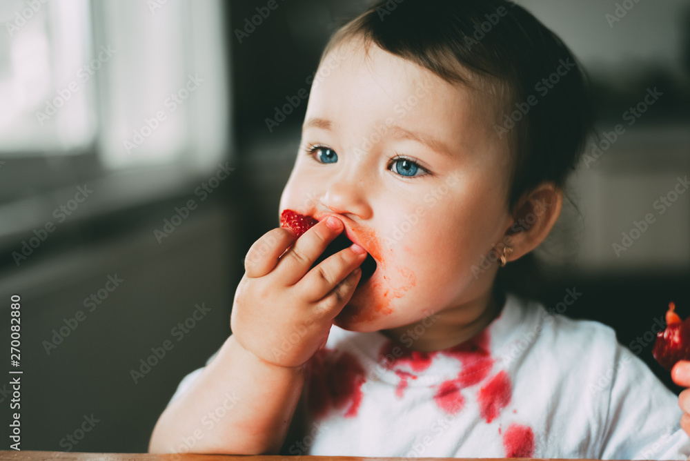 Little girl child in white t-shirt eating strawberries all smeared and dirty Little girl child in white t-shirt eating strawberries all smeared and dirty