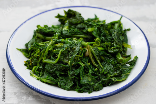 boiled greens with garlic on white plate on ceramic background