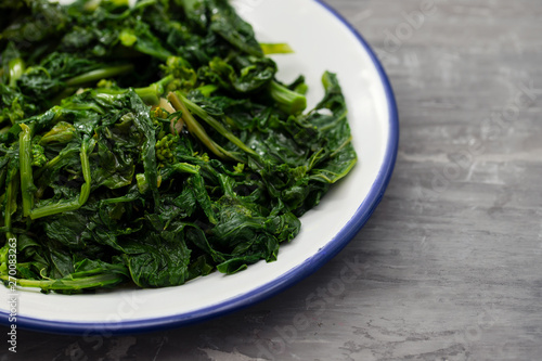 boiled greens with garlic on white plate on ceramic background