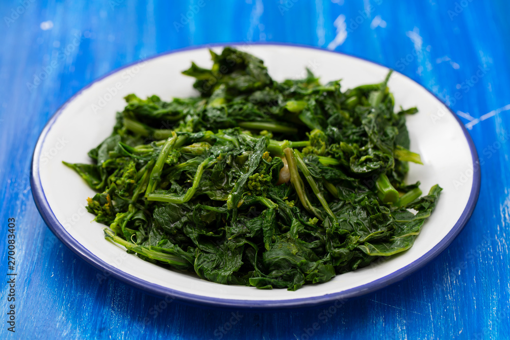boiled greens with garlic on white plate on blue wooden background