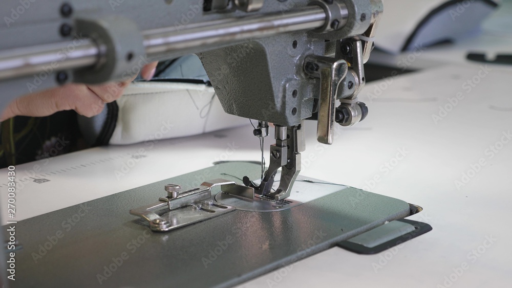 Tailor sews black leather in sewing workshop. needle of sewing machine in motion. process of sewing leather goods. two needles of the sewing machine quickly moves up and down, close-up.