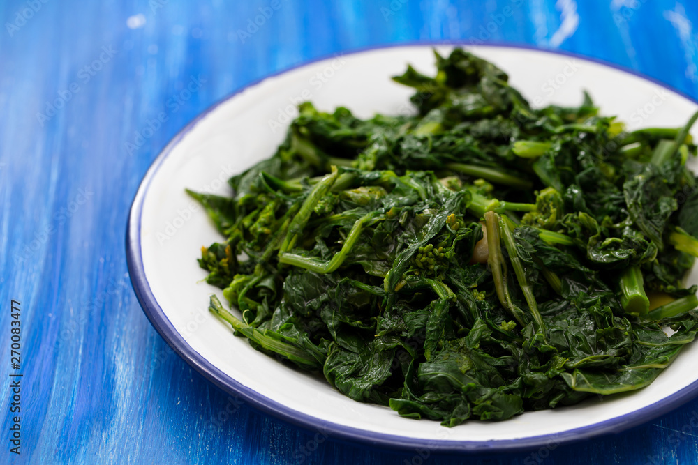 boiled greens with garlic on white plate on blue wooden background