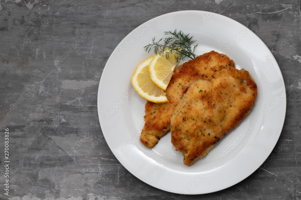 fried chicken with lemon on white plate on ceramic background