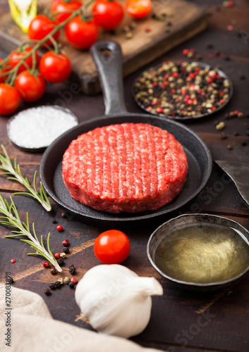 Fresh raw minced homemade farmers grill beef burgers in frying pan with spices and herbs and meat hatchet on wooden board. Oil, garlic and tomatoes.