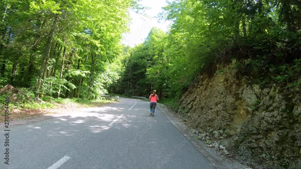 Forward tracking shot of an overweight woman on her daily run up a forest road in sunshine Forward tracking shot of an overweight woman on her daily run up a forest road in sunshine