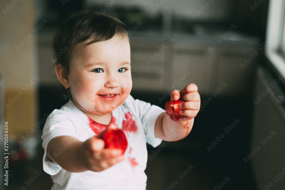 A little girl in a white t-shirt all dirty climbed on the table sitting and eating strawberries A little girl in a white t-shirt all dirty climbed on the table sitting and eating strawberries