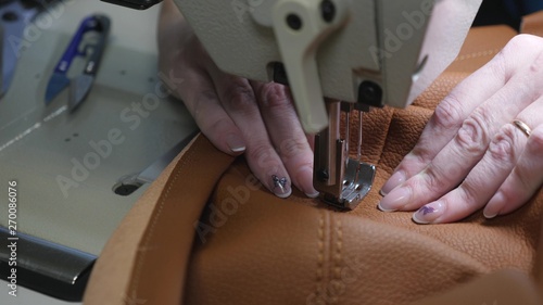 process of sewing artificial leather. needle of sewing machine in motion. two needles of sewing machine quickly moves up and down, close-up. tailor sews brown leather in sewing workshop.