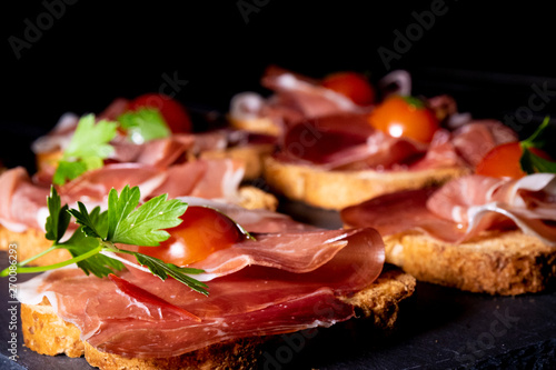 jamón serrano sobre pan tostado con tomate cherry y perejil, en clave oscura y presentado en plato de pizarra photo