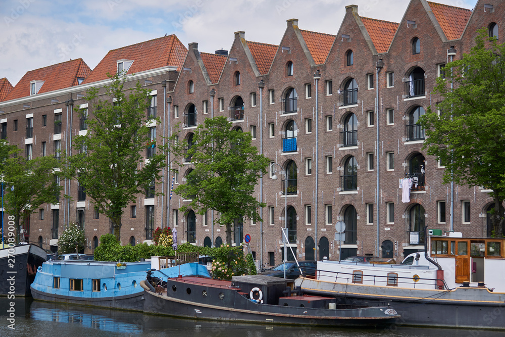 Warehouses with slanted roof in Amsterdam with canal and boats                      