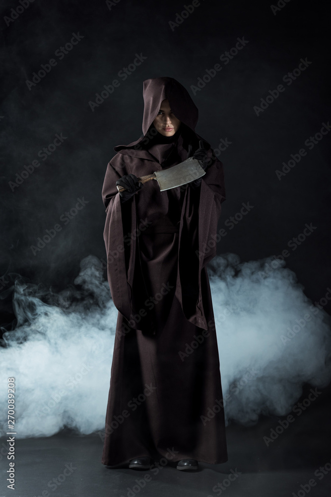 full length view of woman in death costume holding cleaver in smoke on black