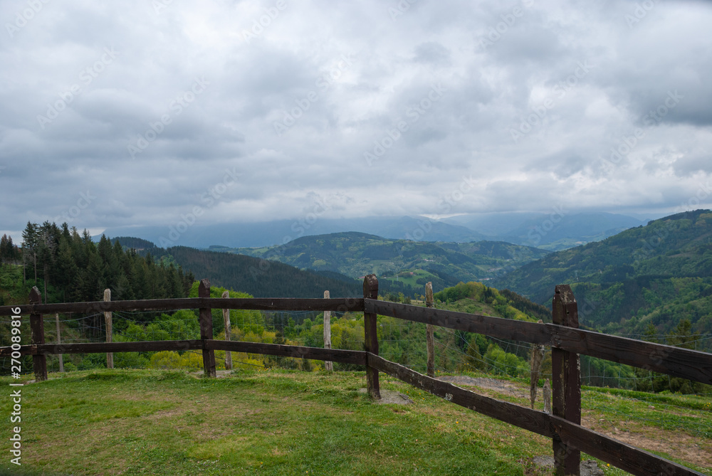 Landscape with green meadows and wooden fence with mountains in the background and cloudy sky in Albiztur, Basque Country, Spain, Europe