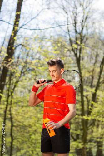 The man pose with a tennis racket and orange thermocouple, on the background of green park. Sport concept