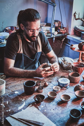 Diligent entusiastic master in glasses at his  pottery studio is workig for a new dish. photo