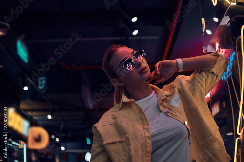 Portrait of pensive trendy woman in neon lights with darkness around.