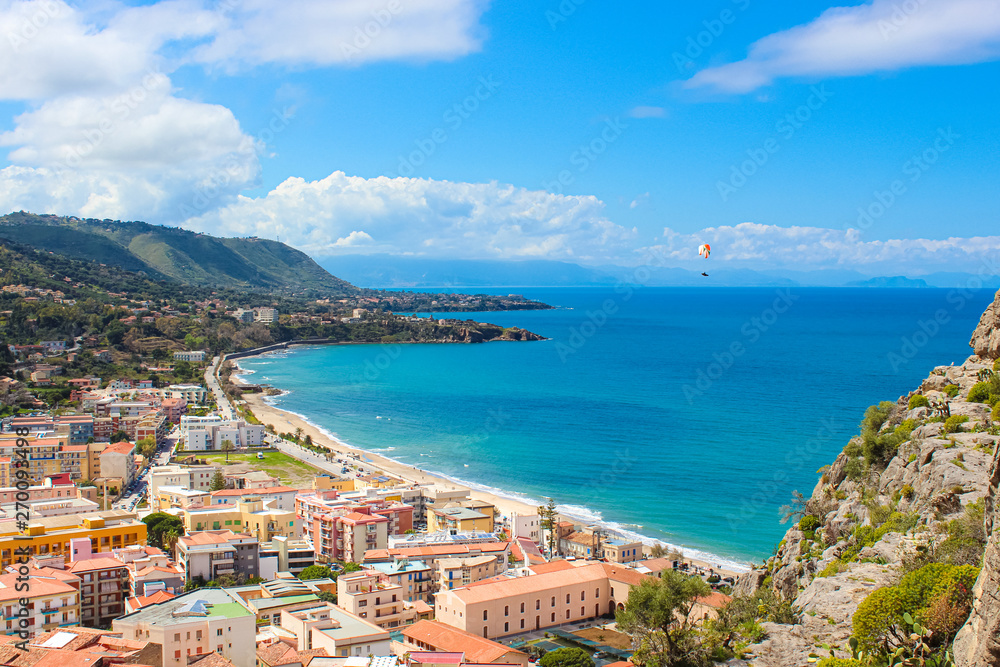 Paraglider flying above the amazing landscape of coastal city Cefalu in beautiful Sicily. Paragliding is a popular extreme sport. Cefalu is one of the major tourist destinations in Italy