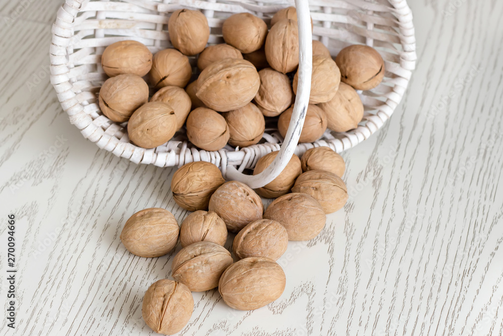Ripe whole walnuts in wicker white small basket on the wood table close-up at selective focus. Ripe whole walnuts in wicker white small basket on the wood table close-up at selective focus.