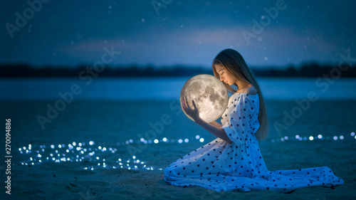 Beautiful attractive girl on a night beach with sand and stars hugs the moon, Artistic Photography