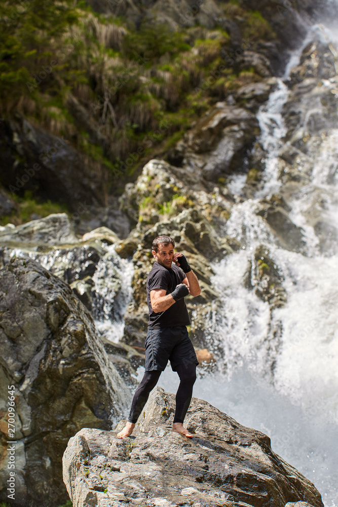 Naklejka premium Muay thai fighter training by the waterfall