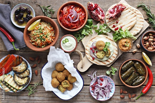Middle eastern, arabic or mediterranean appetizers table concept with falafel, pita flatbread, bulgur and tomato salads, grilled vegetables, stuffed grape leaves,olives and nuts. photo